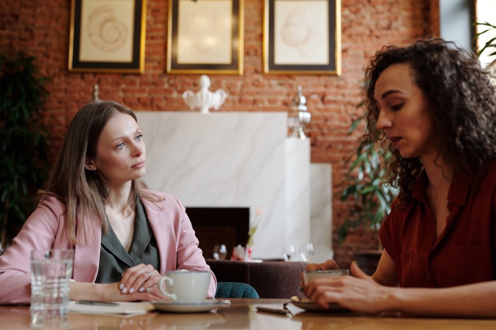 Two adults talking over coffee at a café table.